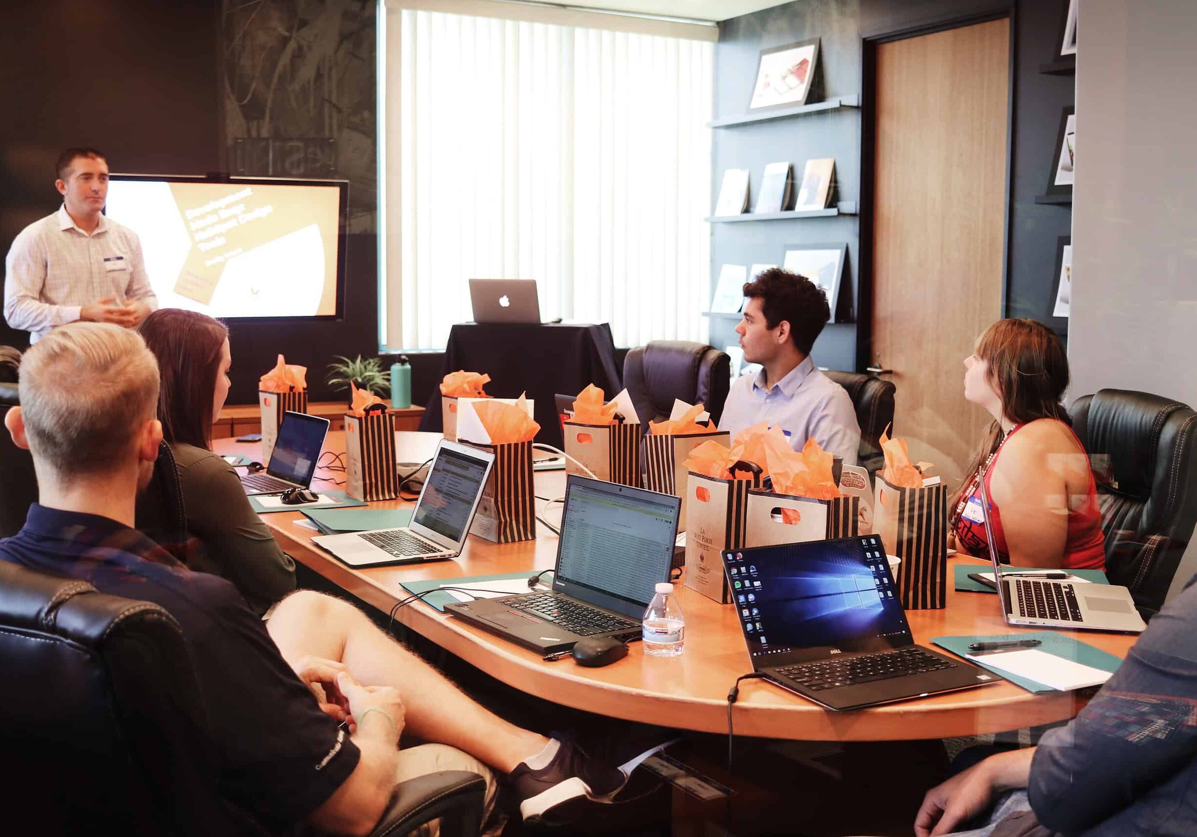 a group of people sitting around a table with laptops